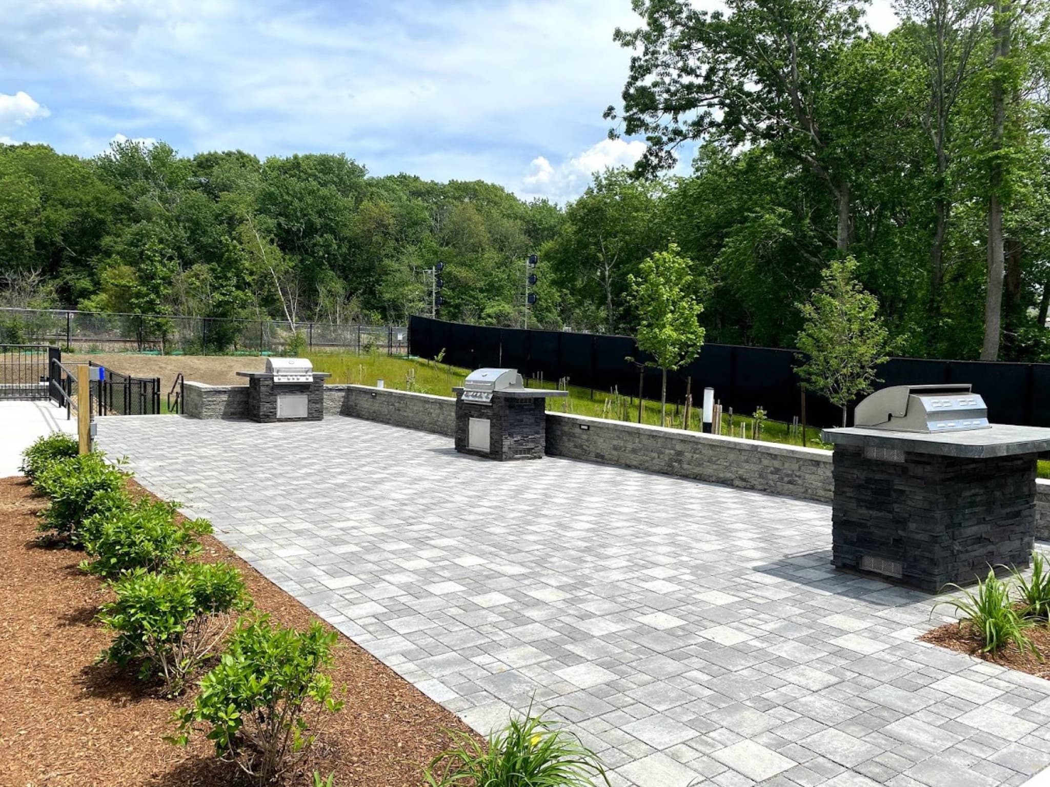 Paver patio with stone seating walls and grill stations at The Point at Weymouth — Hynes Landscaping hardscape